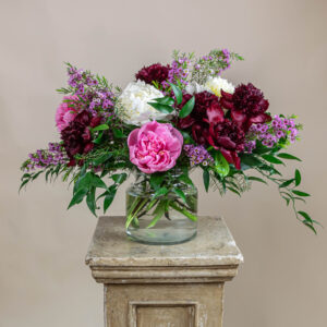 Arreglo Peony Kisses con peonías rojo vino, salmón y blancas, wax flower y ruscus en florero de vidrio, ideal para el Día de las Madres